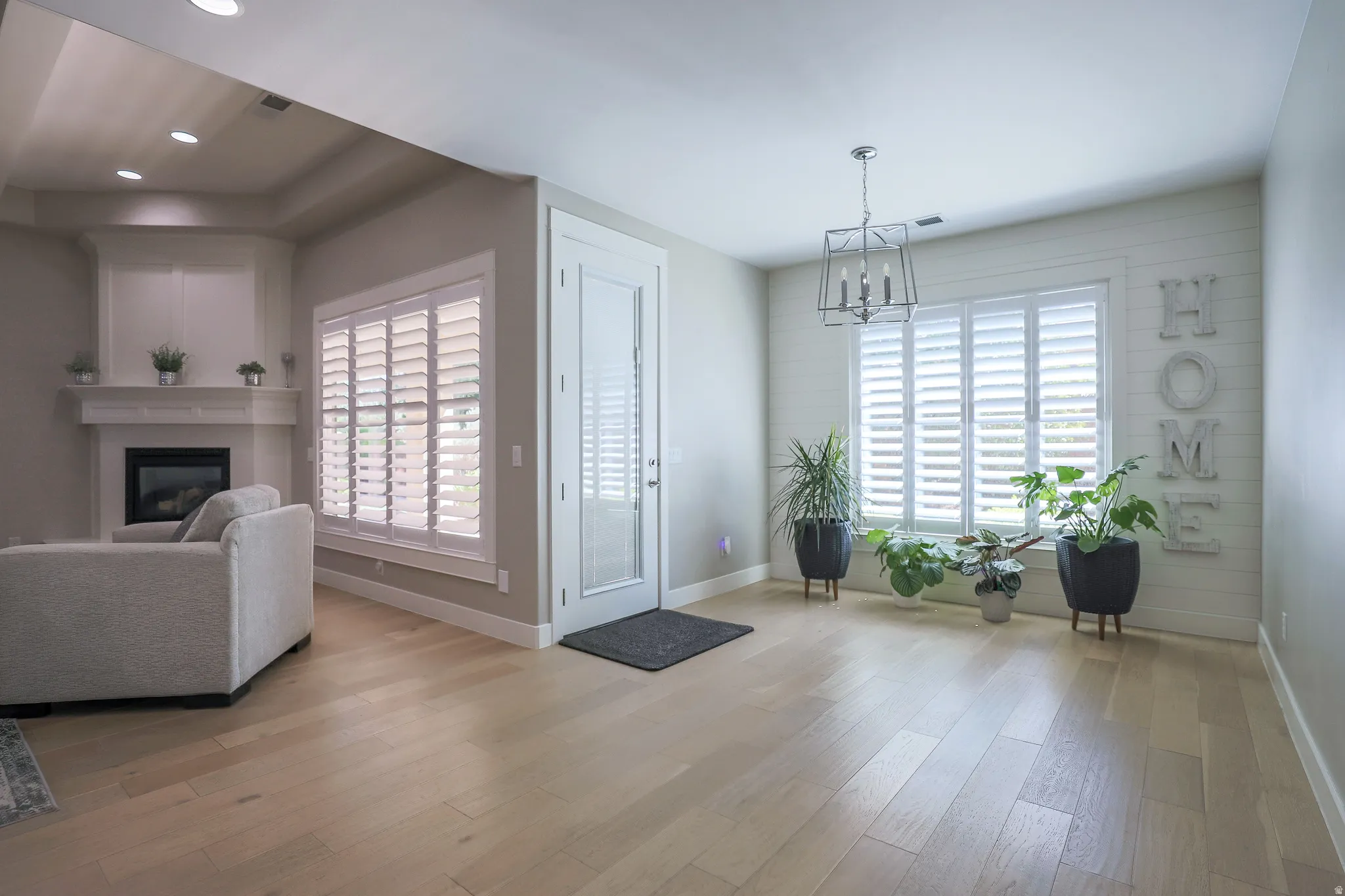 Open-concept living area with light wood-finish flooring, a built-in fireplace featuring a white mantel, and recessed lighting