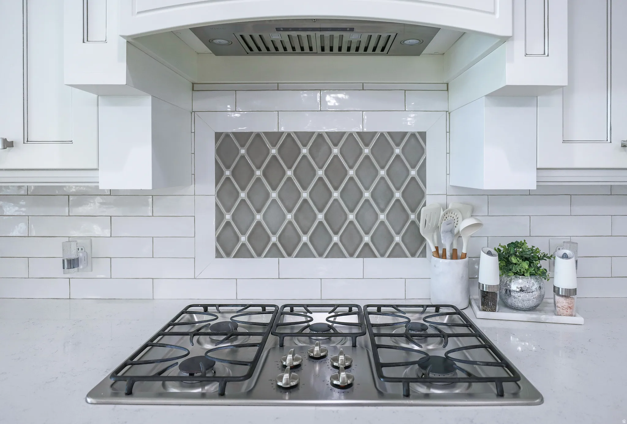 Stainless steel gas cooktop set within a light-toned countertop, featuring a subway tile backsplash