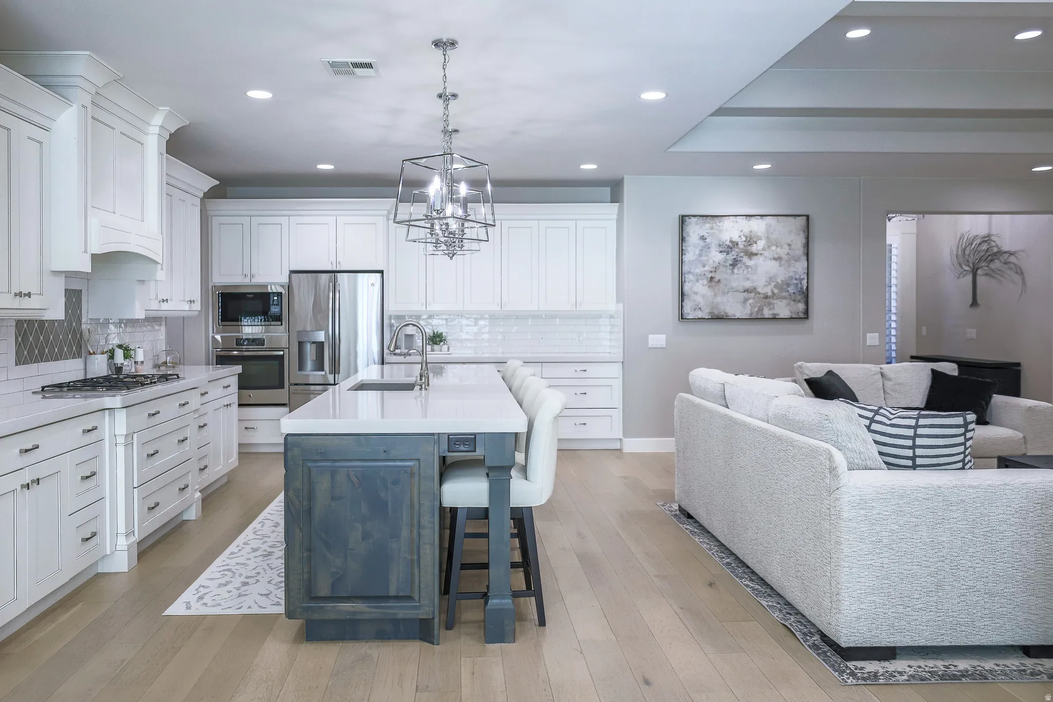 Open-concept kitchen featuring white shaker cabinetry, stainless steel appliances, a center island with seating, and wood-finish flooring