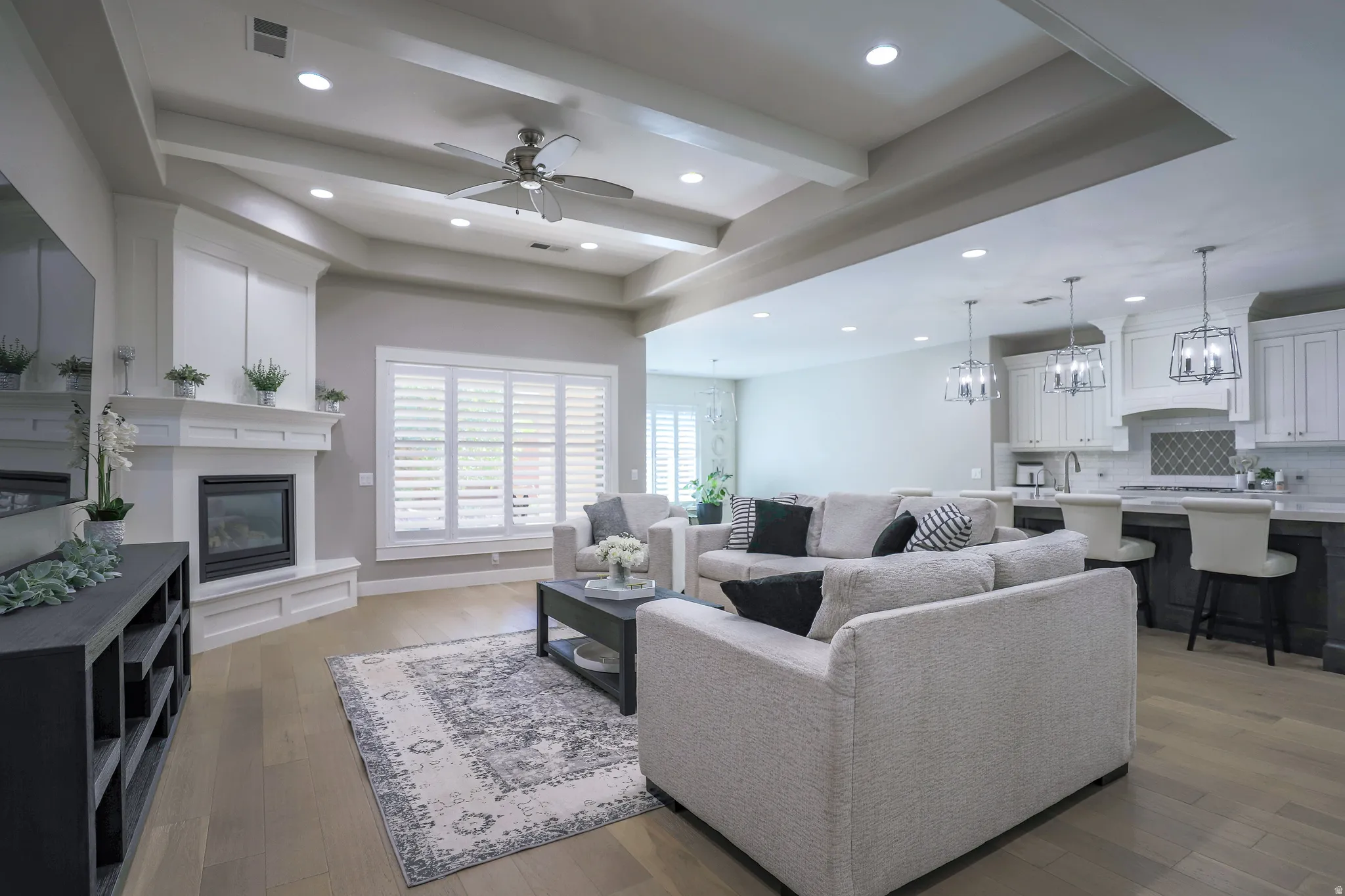Spacious living area featuring a central fireplace with an ornate white mantel, wood-finish flooring, and white plantation shutters