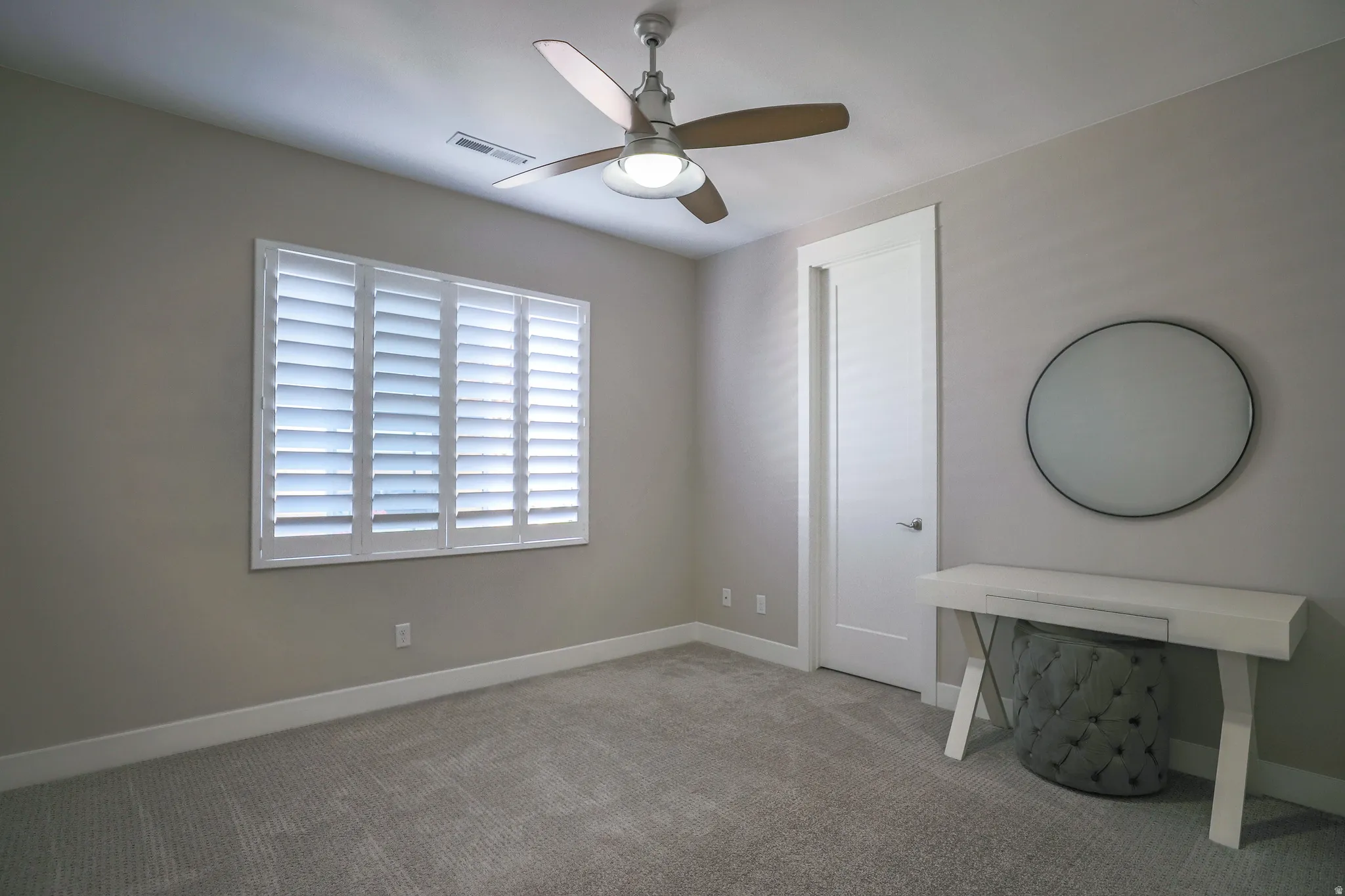 Carpeted interior space featuring a ceiling fan with integrated lighting, a window with plantation shutters, white baseboards, and a modern interior door with white trim