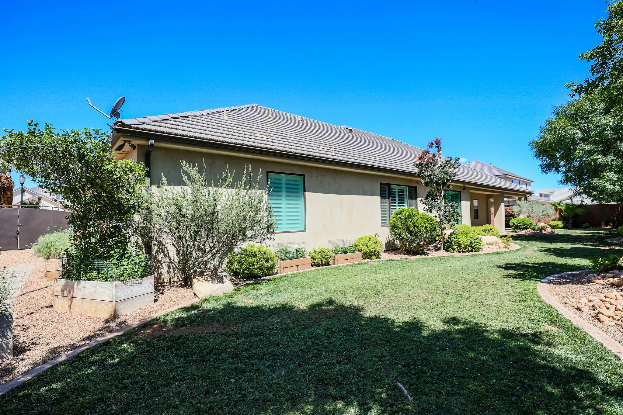 Expansive backyard featuring a manicured lawn, established landscaping, and a covered patio area