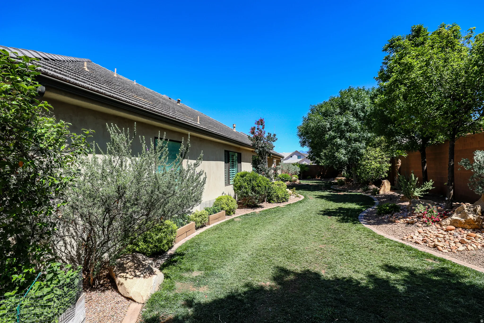 Manicured lawn with mature trees, established landscaping, decorative rock beds, and a stucco exterior