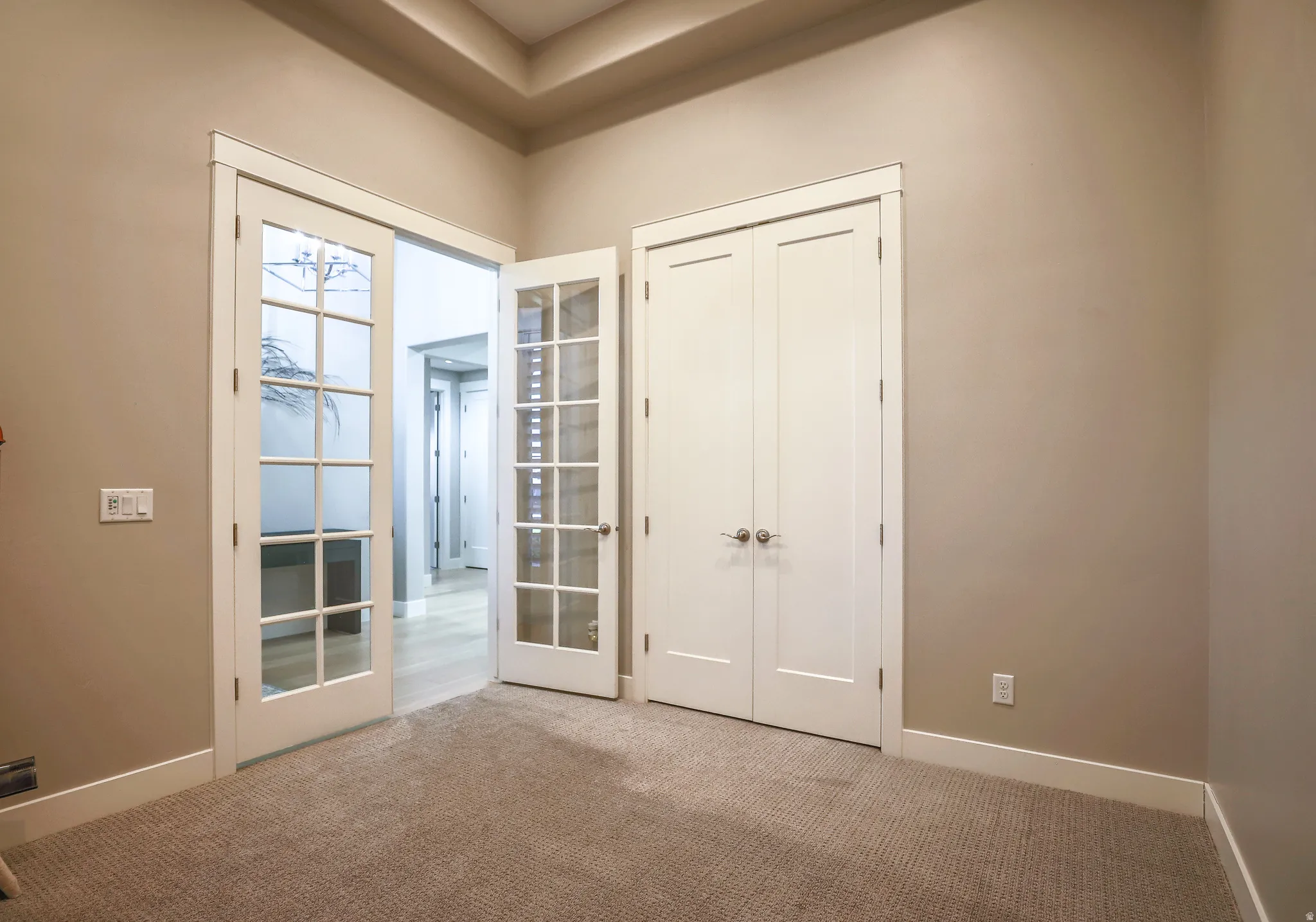 Room featuring dual French doors with glass panes, a tray ceiling, and neutral-toned wall paint