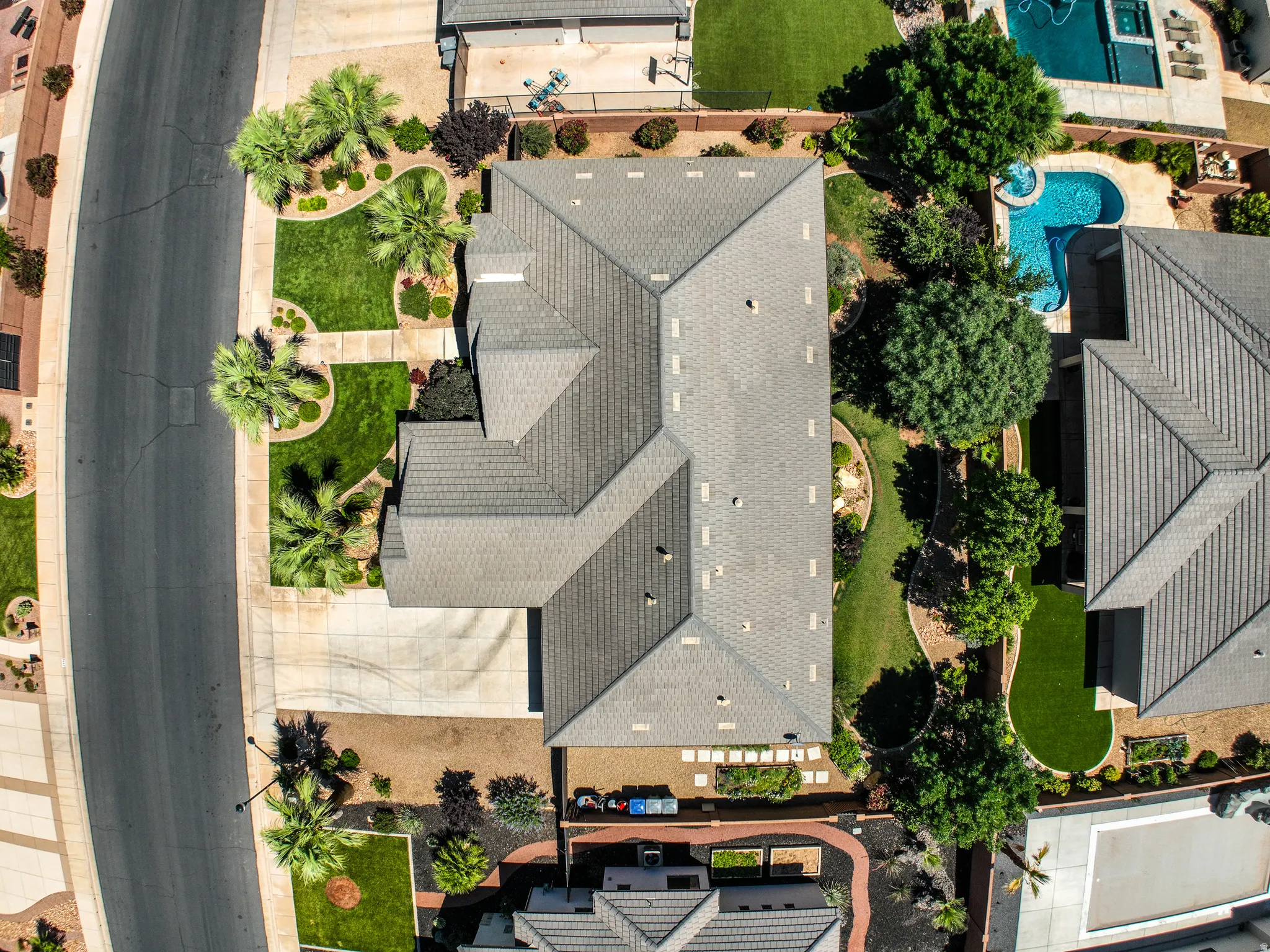 Expansive property featuring a multi-gabled roofline, lush front yard landscaping with palm trees and manicured lawns, a lengthy driveway, and a private rear yard with a swimming pool and additional landscaping