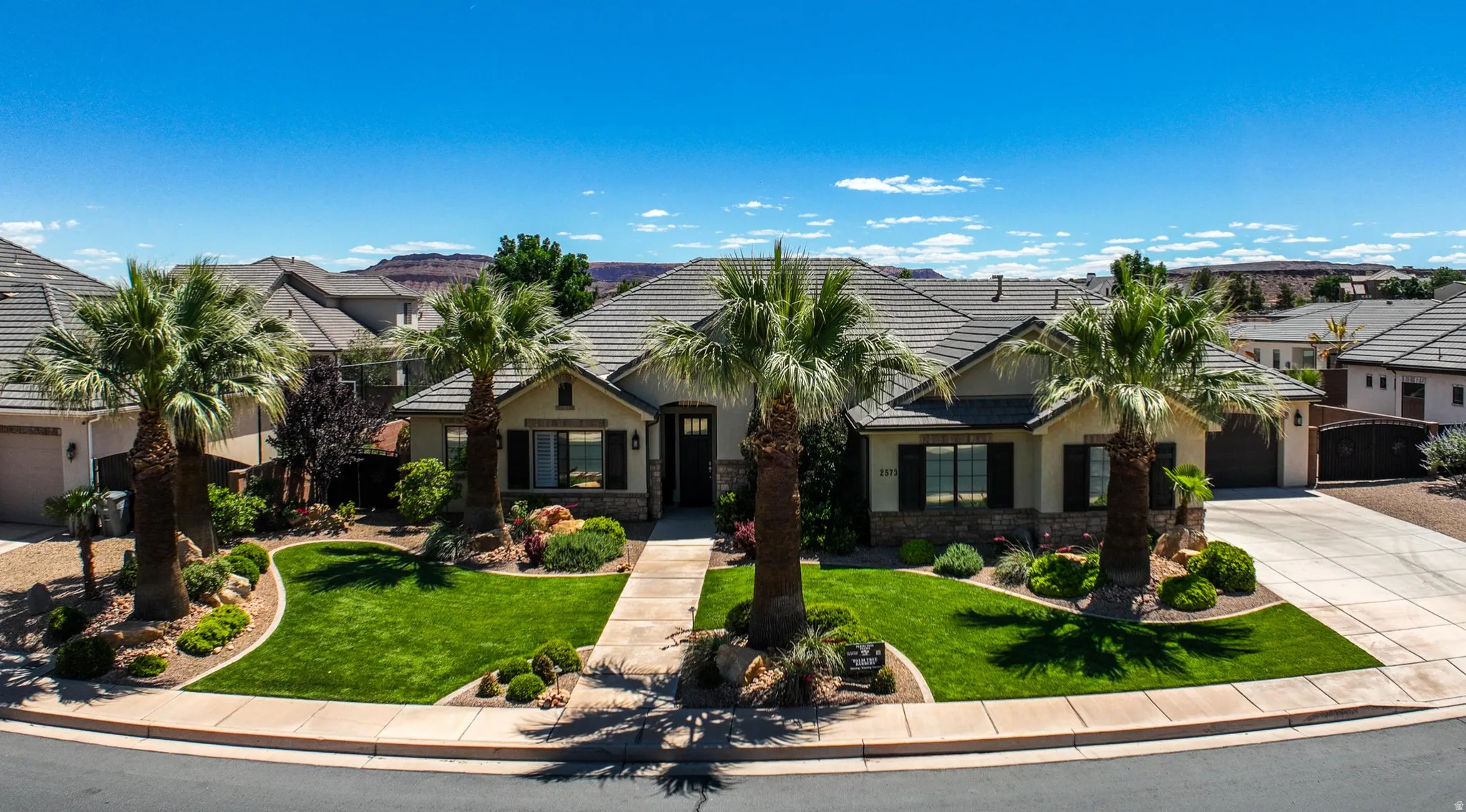 Front exterior featuring a tiled roof, stone accents, manicured lawn, established palm trees, and an integrated two-car garage