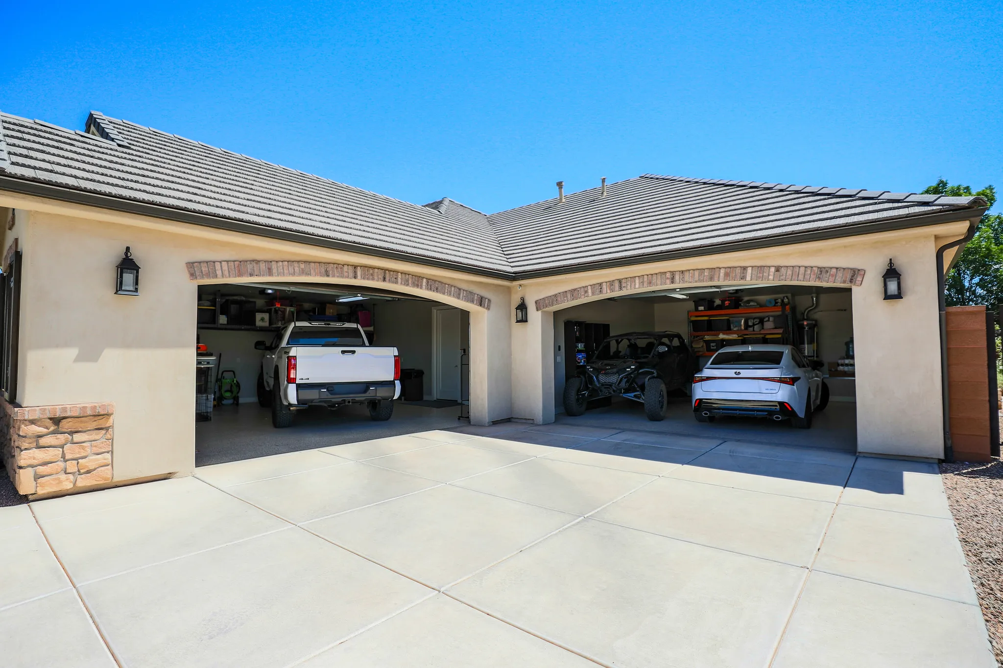 Three-car garage with arched brick detailing over each bay, concrete driveway, and exterior wall lanterns