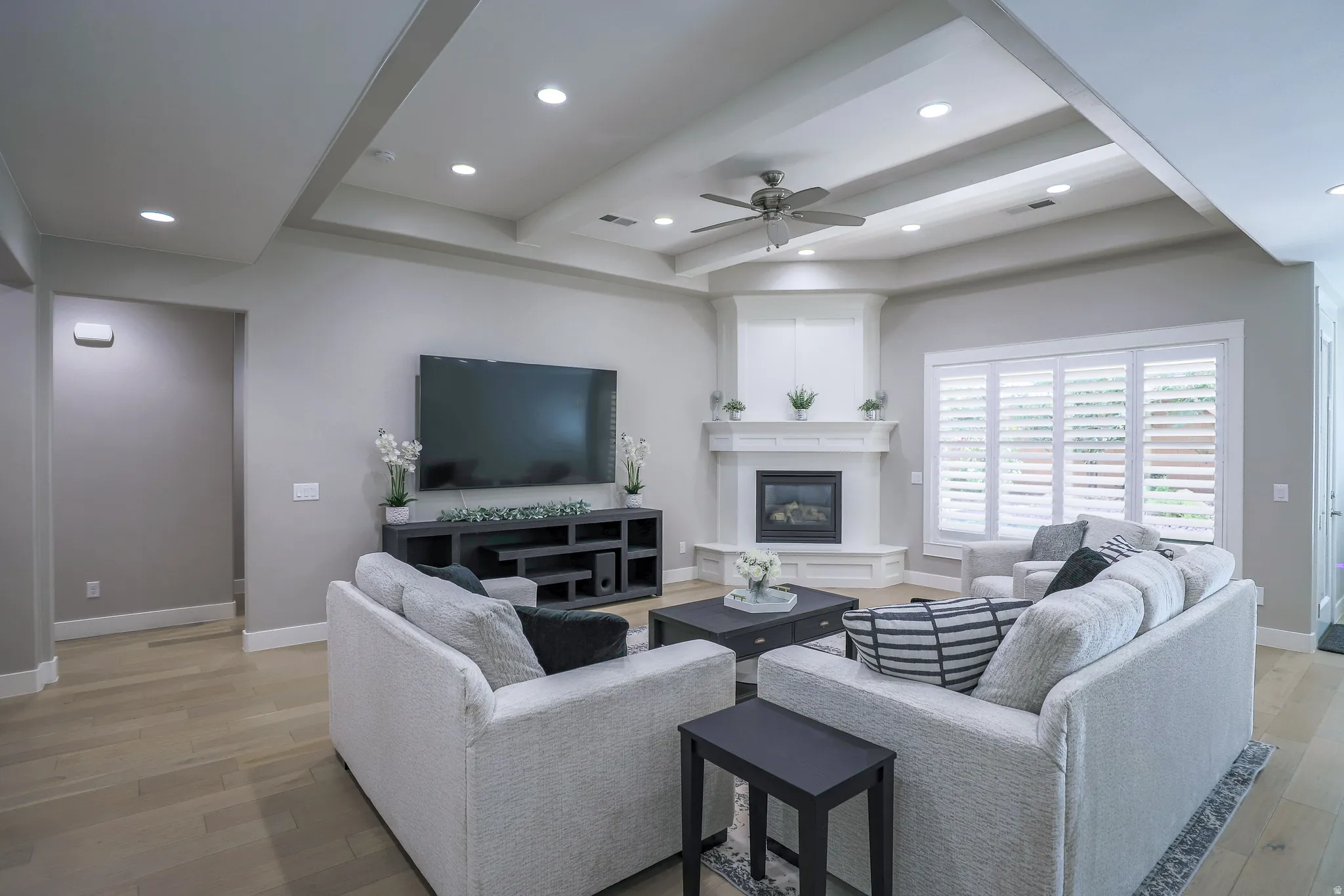 Living area featuring wood-finish flooring, a tray ceiling with recessed lighting, and a corner fireplace with white mantel and hearth