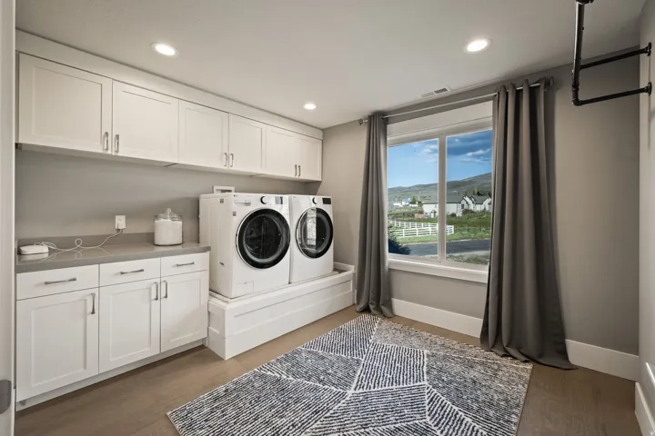 Spacious laundry room with ample white cabinetry, integrated countertop, wood-finish flooring, and a large window