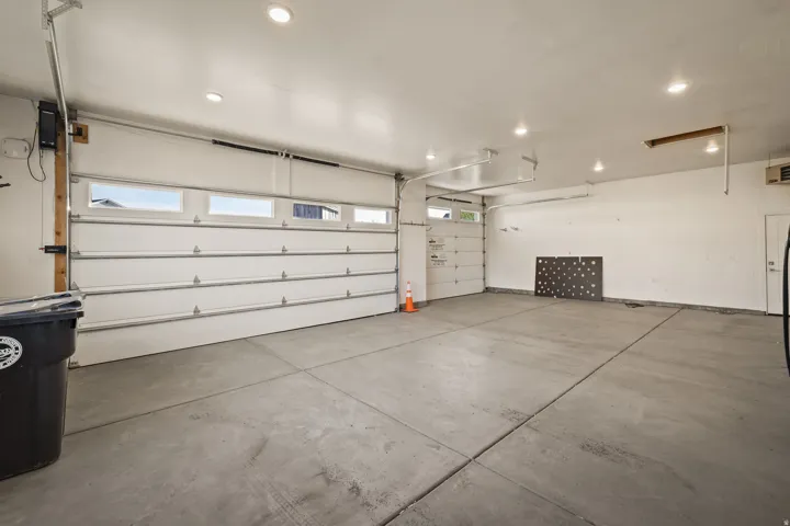 Spacious garage featuring a concrete floor, two white overhead garage doors with windows, and recessed lighting