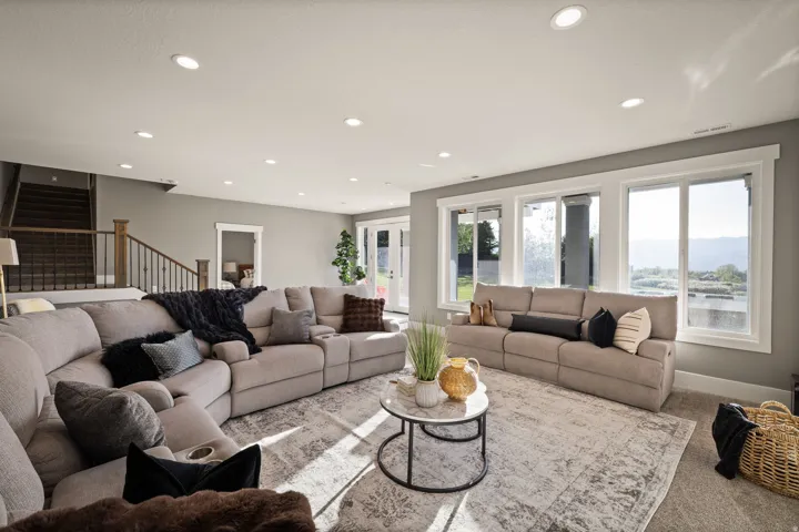 Spacious living area featuring large windows, recessed lighting, neutral wall tones, a carpeted floor, and a staircase with wood and metal railing