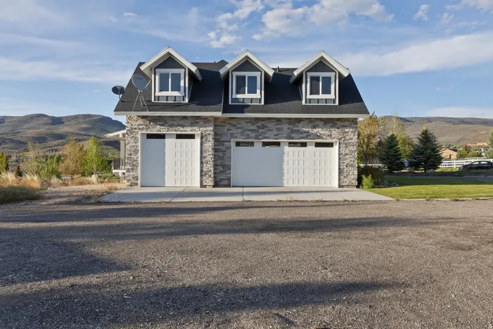 Detached two-car garage featuring stone veneer siding, a dark shingle roof, and three dormer windows