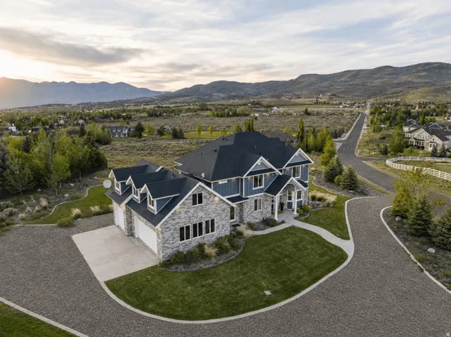 Contemporary two-story residence featuring a blue siding and stone exterior, a multi-car garage, and a lush green lawn