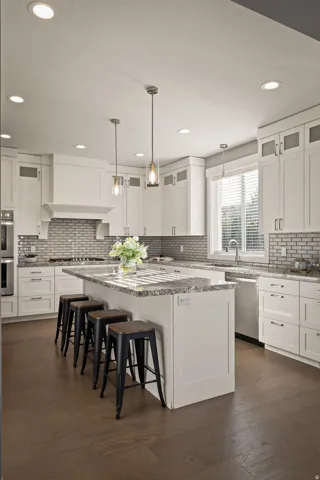 Bright kitchen featuring an expansive center island with seating, white shaker cabinetry, stainless steel appliances, and wood-finish flooring