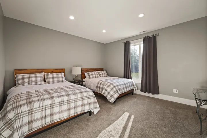 Spacious bedroom featuring light gray walls, plush carpet flooring, recessed lighting, and a large window with white trim