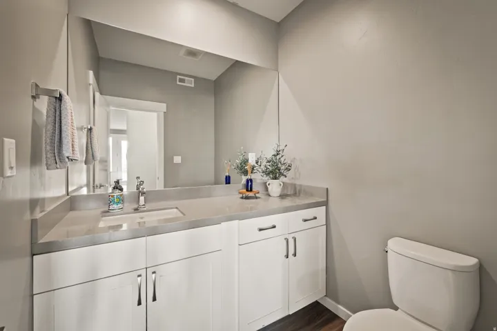 Bathroom featuring an integrated countertop and sink, white cabinetry with silver-tone hardware, a wall-mounted mirror, and wood-finish flooring