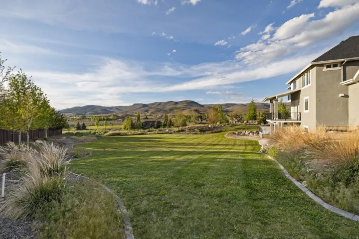 Expansive grassy lawn bordered by mature trees and decorative grasses