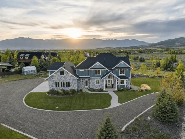 Contemporary home with stone and siding facade, a dark shingle roof, and multiple gables