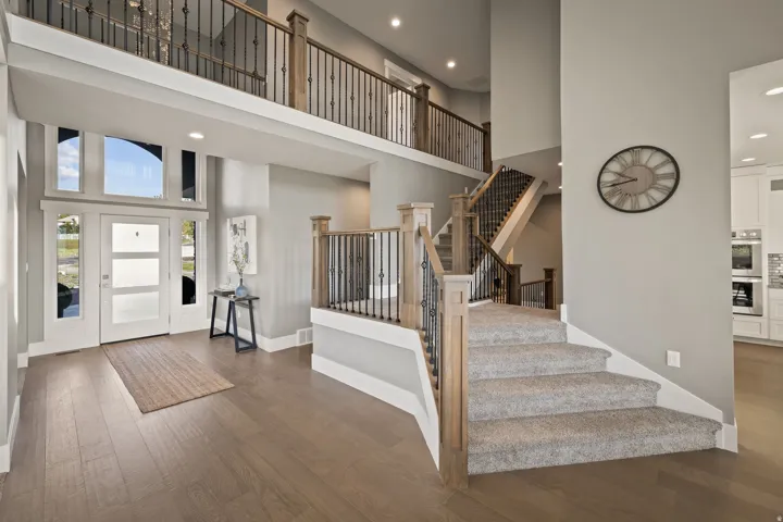 Two-story foyer featuring wood-finish flooring, a contemporary entry door with frosted glass panels, and multiple transom windows