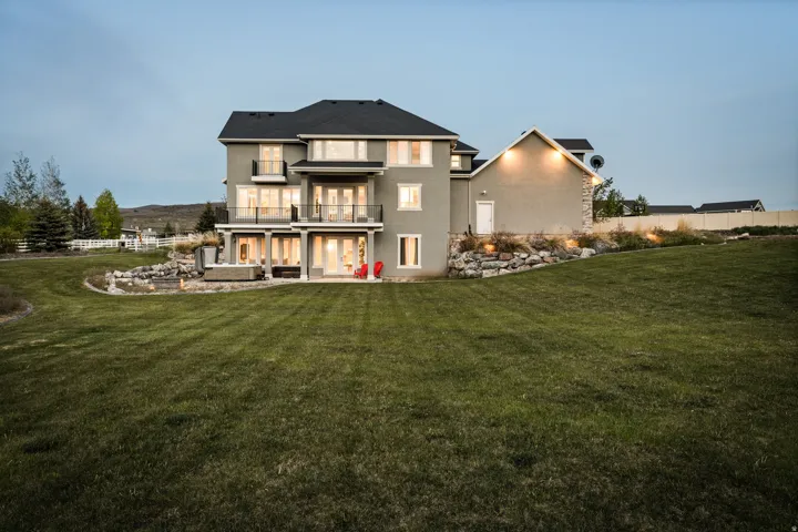 Expansive tiered backyard featuring a large green lawn, a rock retaining wall with integrated lighting, and a paved patio area