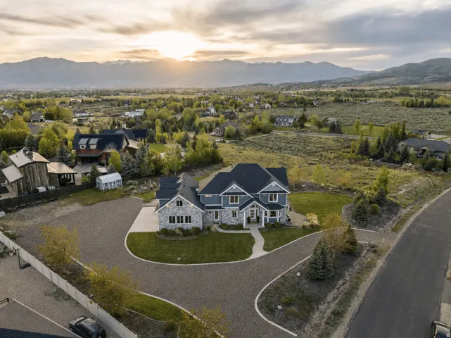 Custom-built residence featuring stone and siding exterior, a dark shingle roof, and an expansive gravel driveway