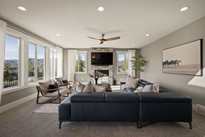 Spacious living room featuring a stone-clad fireplace, recessed lighting, and a wood-finish ceiling fan