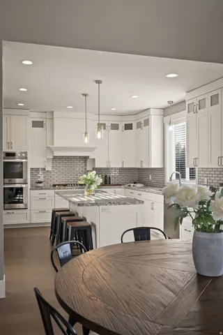 Modern kitchen featuring white cabinetry, granite countertops, an integrated oven and microwave, a tile backsplash, and wood-finish flooring