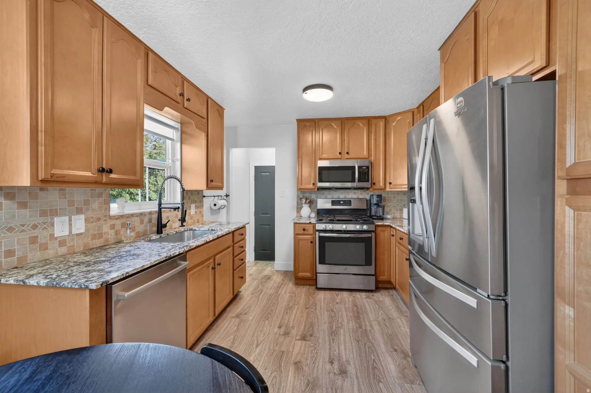 Spacious kitchen featuring wood cabinetry, stainless steel appliances, granite countertops, tile backsplash, and wood-finish flooring