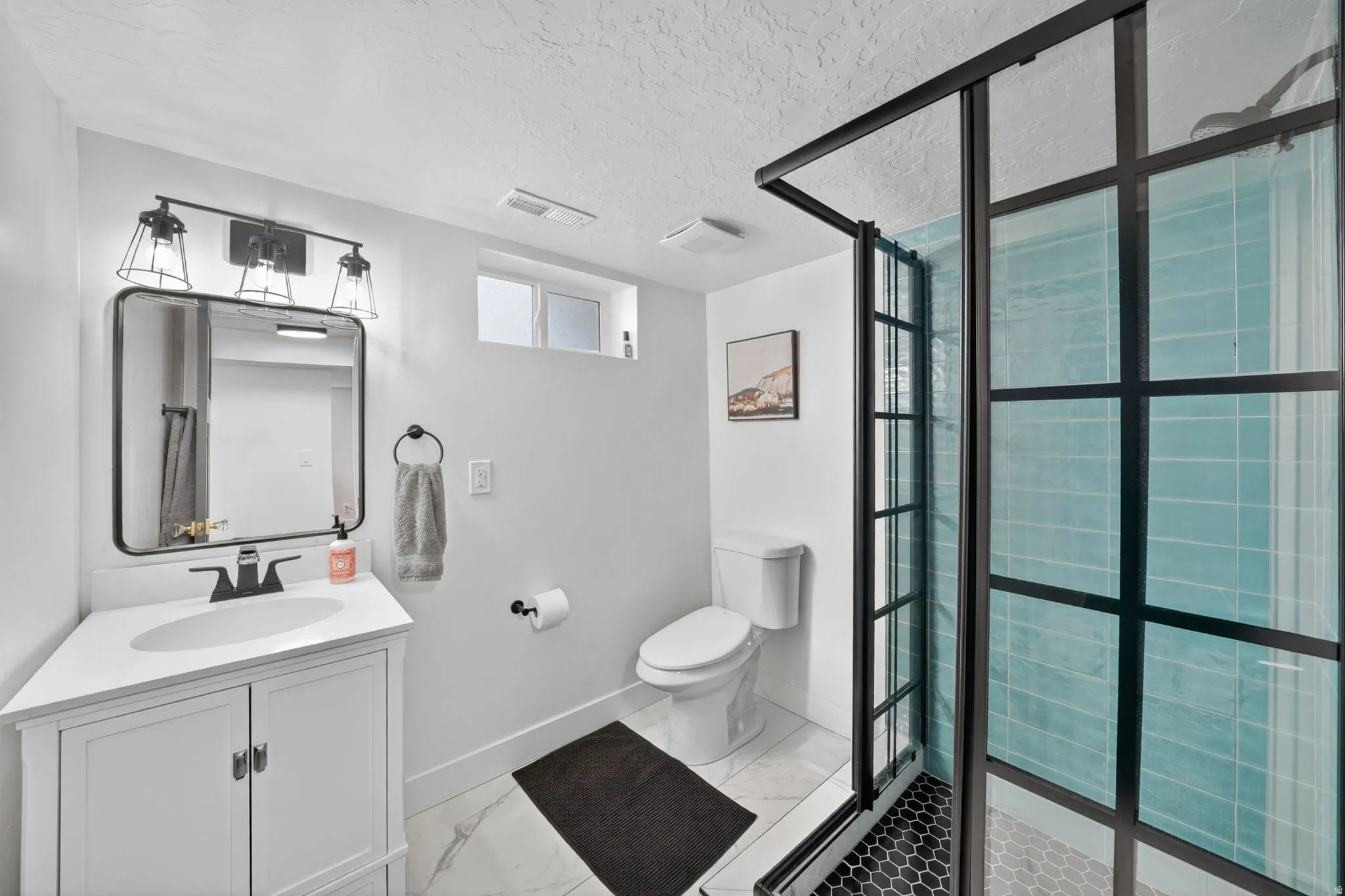 Bathroom featuring a black-framed glass shower enclosure with blue subway tile, white vanity with integrated sink and quartz-finish countertop, black hardware throughout, and white tile flooring