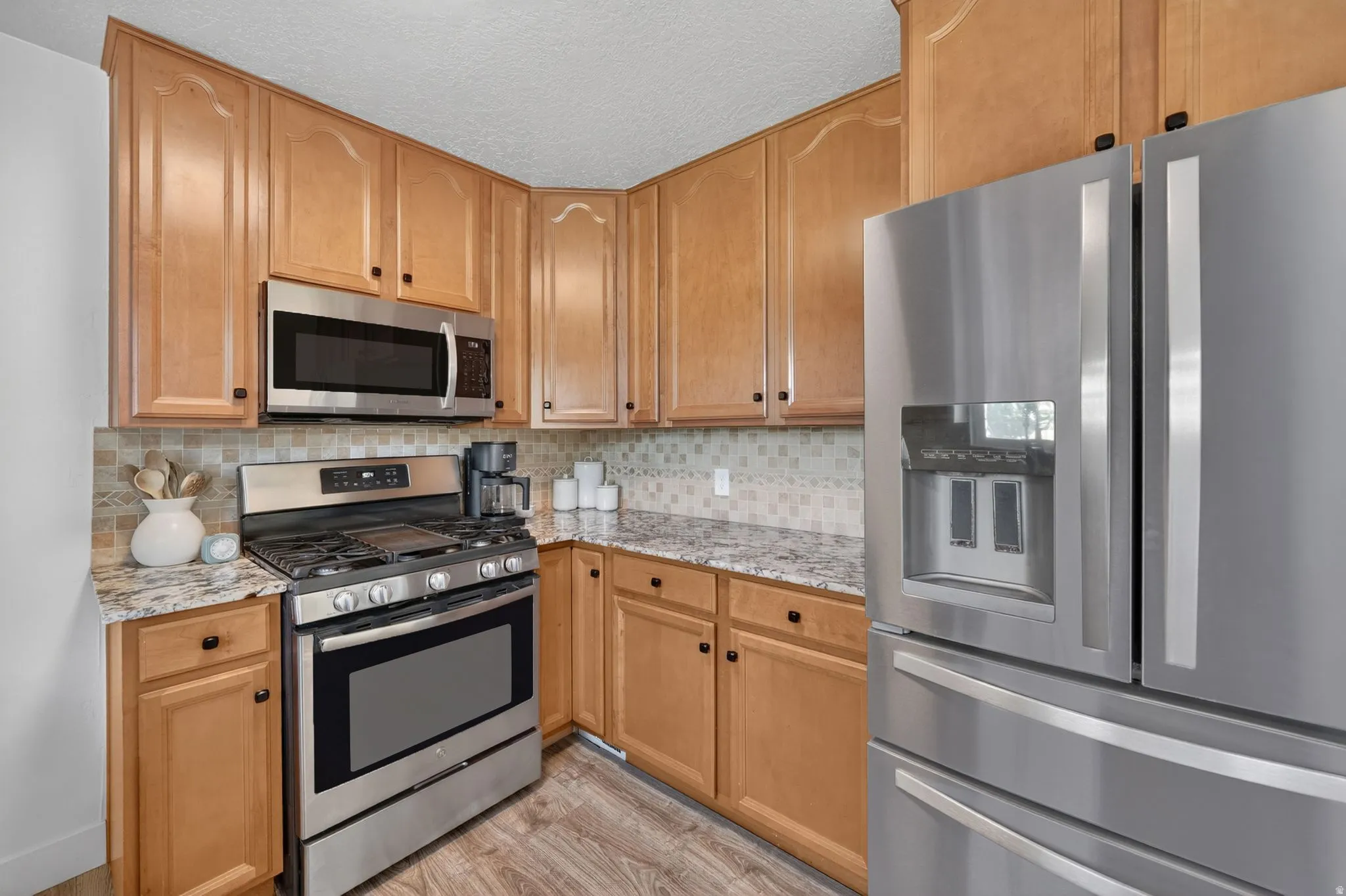 Kitchen featuring wood cabinetry, stainless steel appliances, speckled countertops, a mosaic tile backsplash, and wood-finish flooring