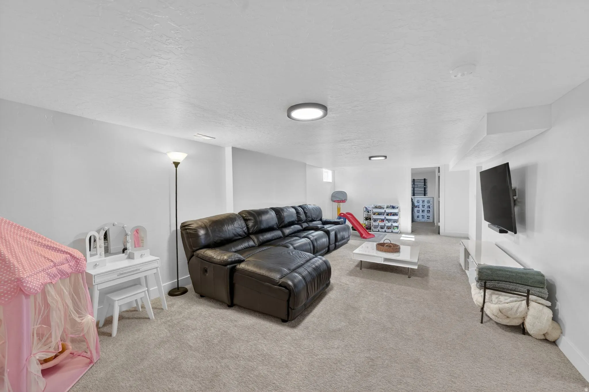 Spacious lower-level entertainment area featuring recessed lighting, light-toned carpeting, and a wall-mounted television