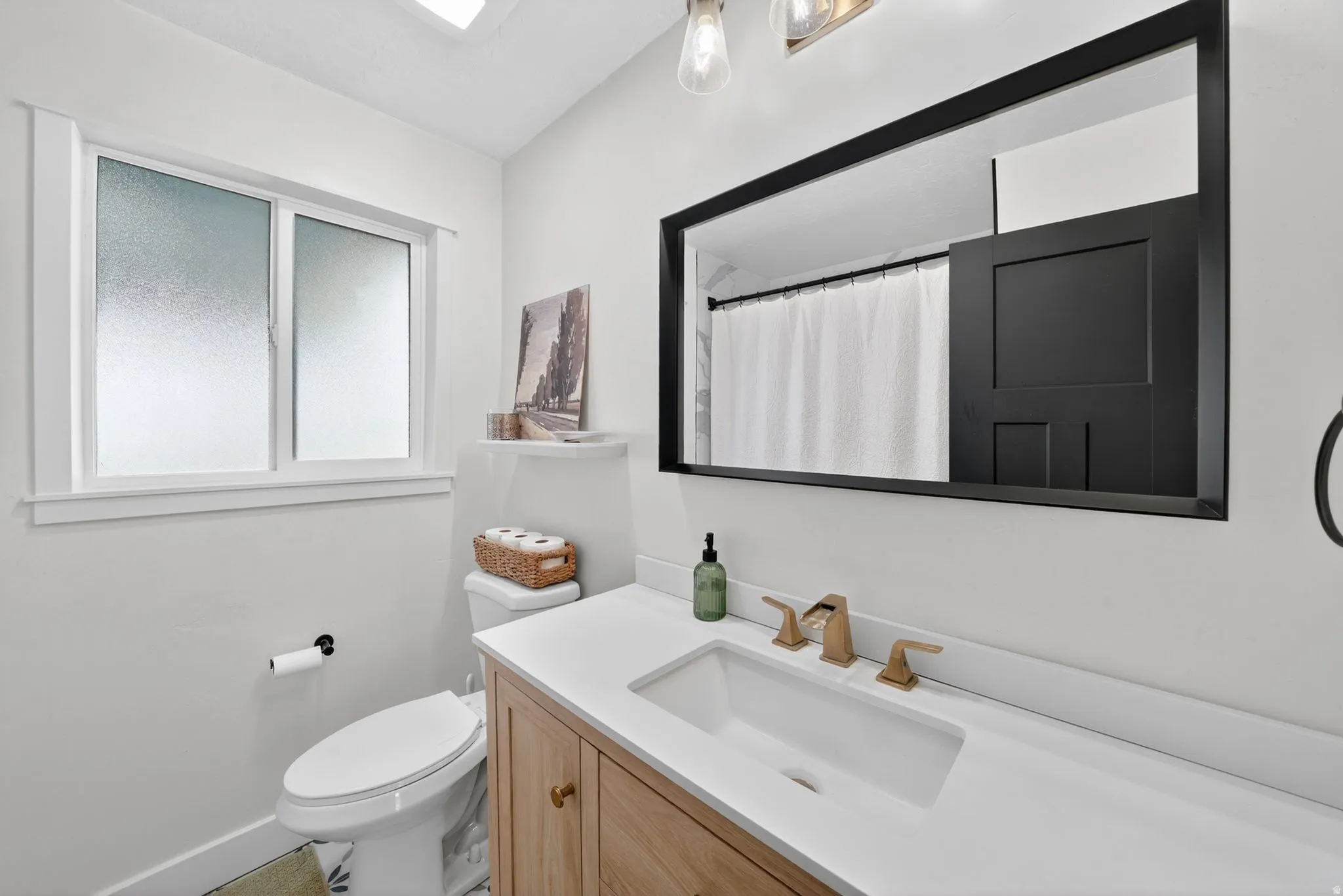 Modern bathroom vanity with a single basin, gold-finish faucet, and a large black-framed mirror