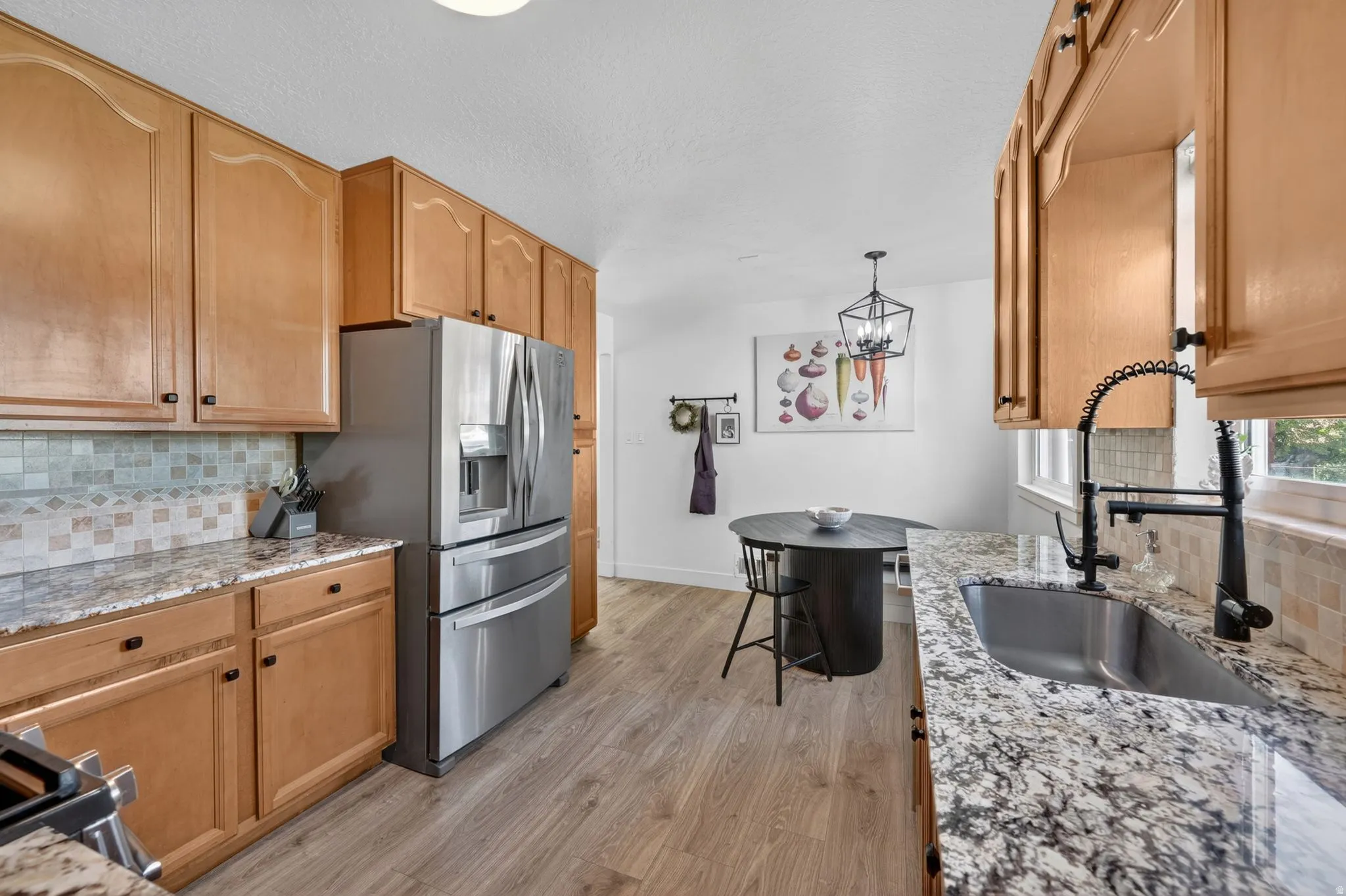 Kitchen featuring light wood cabinetry, granite-style countertops, mosaic tile backsplash, and stainless steel appliances