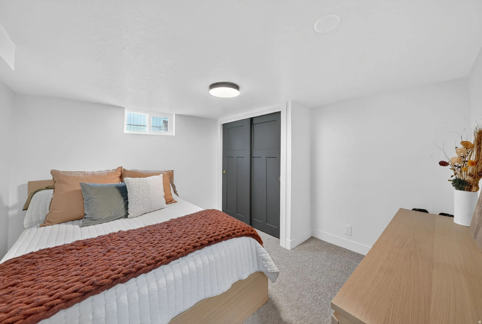Bedroom featuring light gray carpeting, crisp white walls, a recessed window, black sliding closet doors, and a ceiling-mounted light fixture