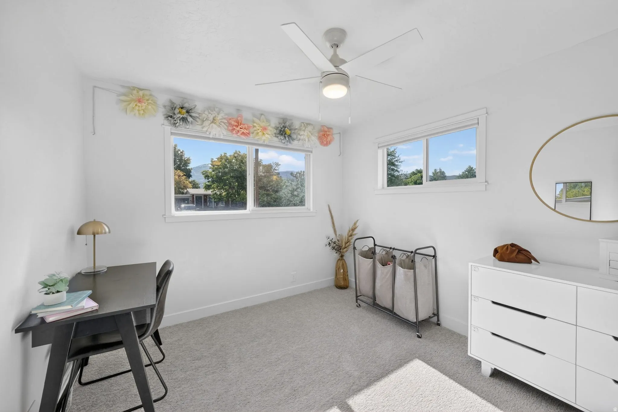 Bright room featuring two windows, neutral carpeting, a ceiling fan with integrated lighting, and white painted walls