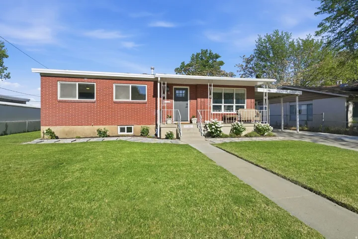Brick exterior with a covered front porch featuring white railing, a concrete walkway, and a manicured lawn