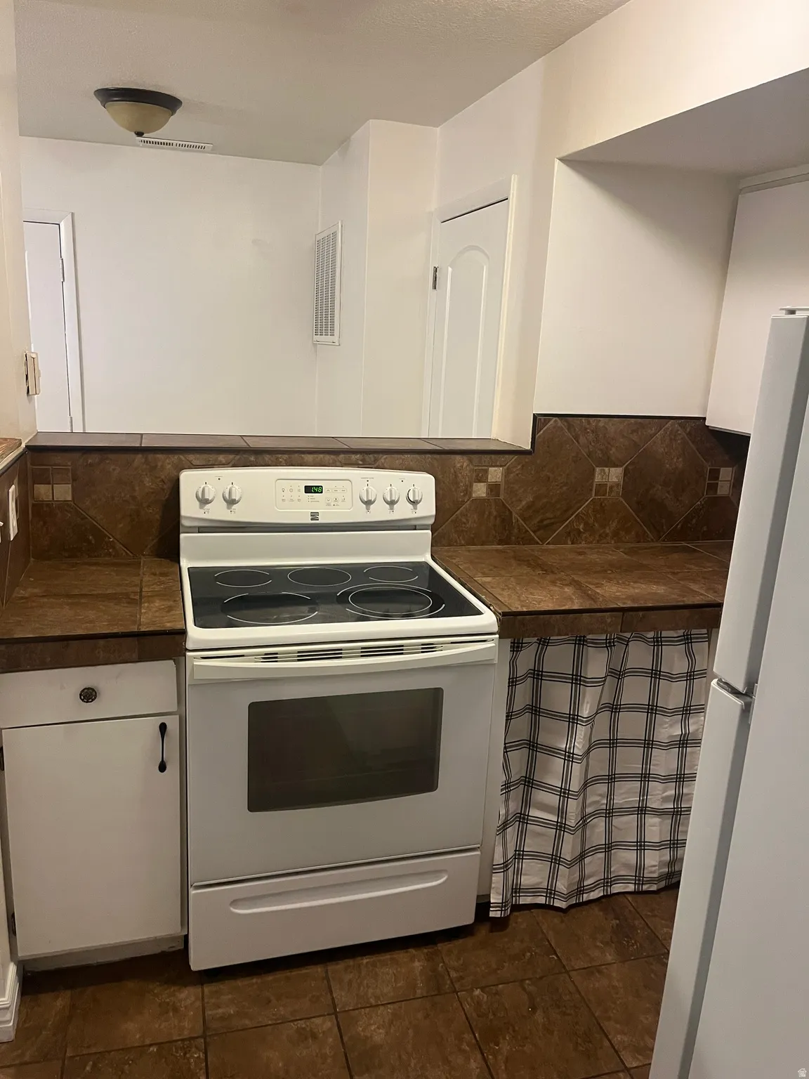 Kitchen featuring a white electric range, dark tile flooring, and a coordinating dark tile backsplash