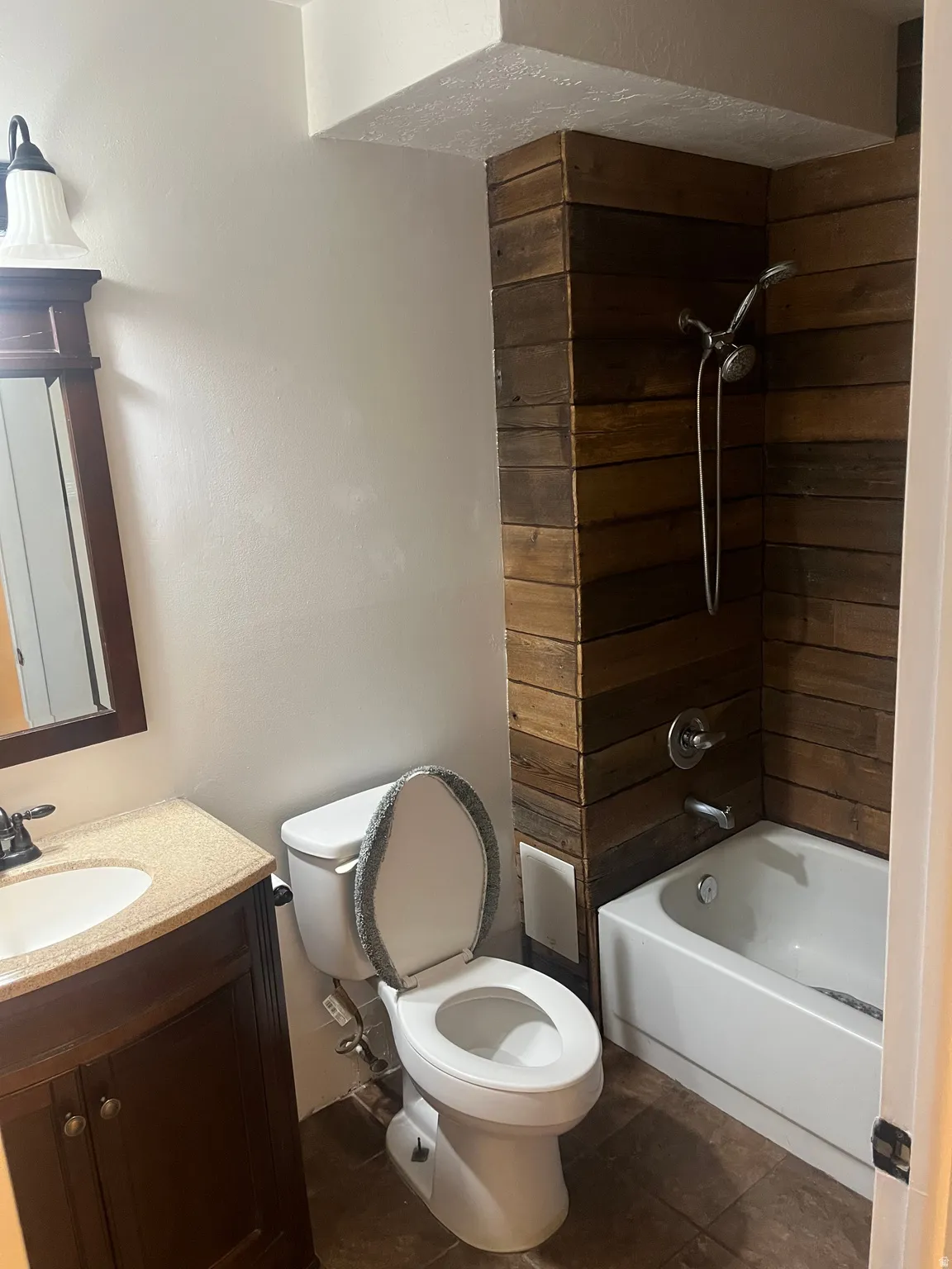 Bathroom featuring a wood-panel accent wall, white bathtub with a chrome shower fixture, and a dark wood-finish vanity with a light-toned countertop and integrated sink