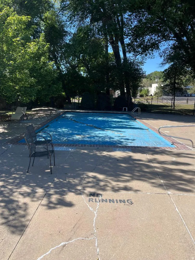 Outdoor pool area featuring a blue pool cover, surrounding concrete deck, and mature trees providing shade