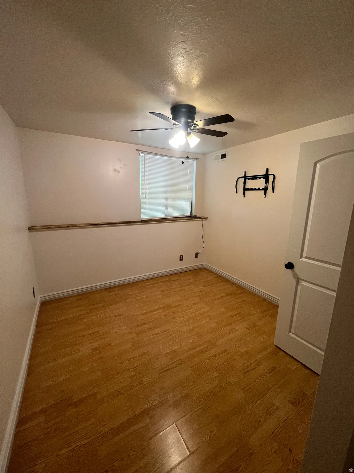 Room featuring wood-finish flooring, a ceiling fan with integrated lighting, a window with horizontal blinds, and a paneled door with black hardware