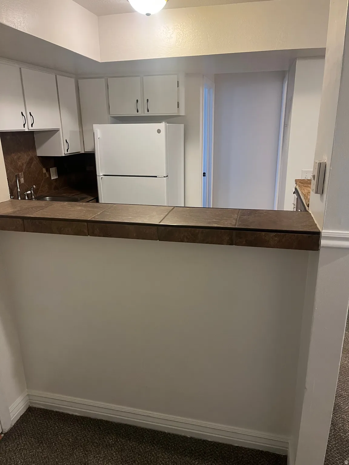 Kitchen featuring white cabinetry, a built-in sink, a refrigerator, and a tiled breakfast bar