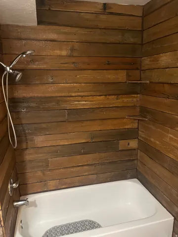Bathtub and shower combination featuring wood-finish wall paneling, a chrome showerhead with a flexible hose, and coordinating chrome fixtures