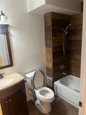 Bathroom featuring a wood-panel accent wall, white bathtub with a chrome shower fixture, and a dark wood-finish vanity with a light-toned countertop and integrated sink