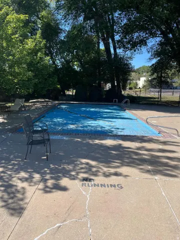 Outdoor pool area featuring a blue pool cover, surrounding concrete deck, and mature trees providing shade