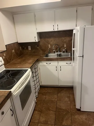 Kitchen featuring white cabinetry, brown tile backsplash, laminate countertops, and tile flooring