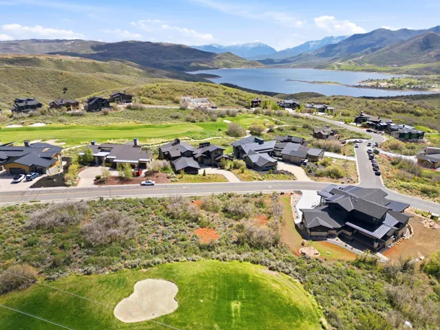 Aerial perspective showcasing a residential community amidst rolling hills with a large body of water and distant mountains