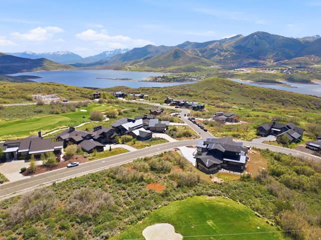 Expansive mountain landscape featuring a large body of water, lush green hillsides, and snow-capped peaks