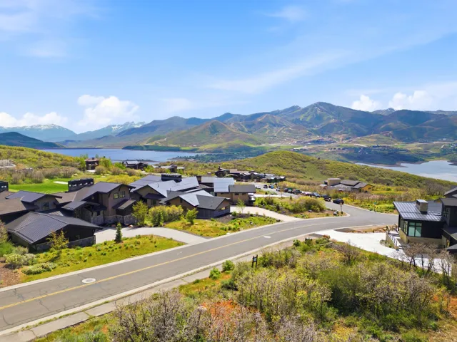 Aerial overview showcasing a cluster of properties with dark roofs, surrounded by green hills, a substantial body of water, and distant mountains