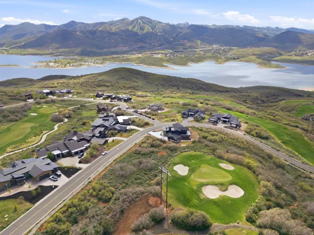 Expansive mountain landscape featuring a large body of water, green golf course, and multiple contemporary residences