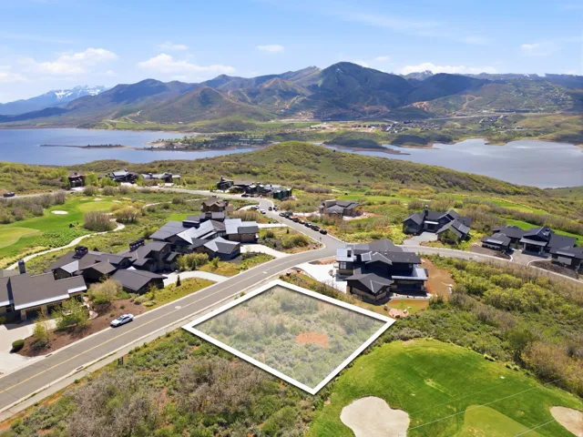 Elevated lot featuring natural vegetation, bordered by a paved road and a manicured golf course, with surrounding residences and distant water and mountain scenery